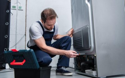 Man in overalls doing repairs on a refrigerator.