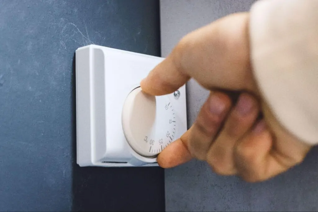 Close-up of a hand adjusting the temperature on a wall-mounted digital thermostat.