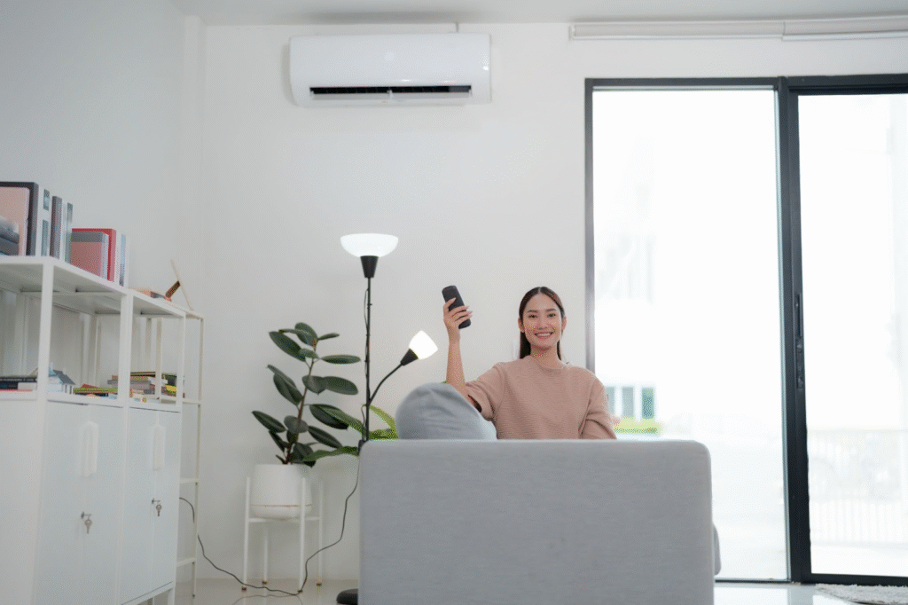 A woman sitting on a couch adjusts a ductless mini split behind her with a remote control.