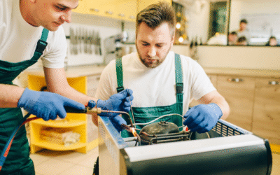 Two appliance technicians repair a refrigerator burner system at a residential unit.