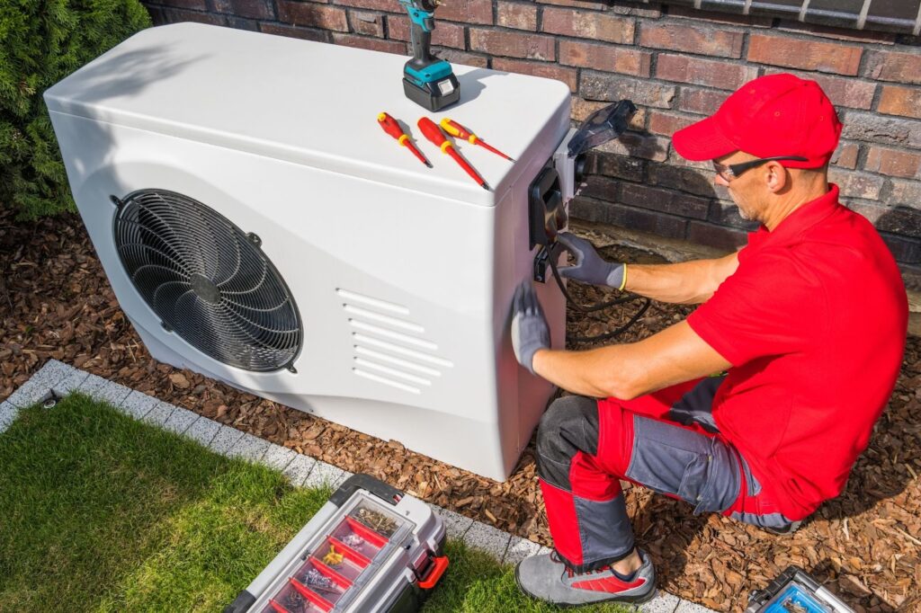 A technician repairs a heat pump unit sitting in a home’s backyard.